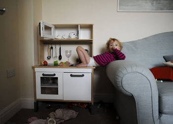 Portrait of girl lying on sofa and toy kitchen counter