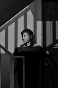 Portrait of young man standing against railing at home