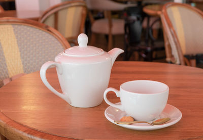 White porcelain teapot and tea cup stand on a table in a cafe