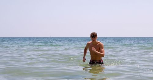 Full length of shirtless man in sea against clear sky