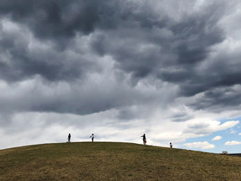 Low angle view of people on hill against storm clouds