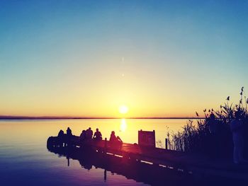 Silhouette people by sea against clear sky during sunset