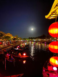 Illuminated city by river against sky at night