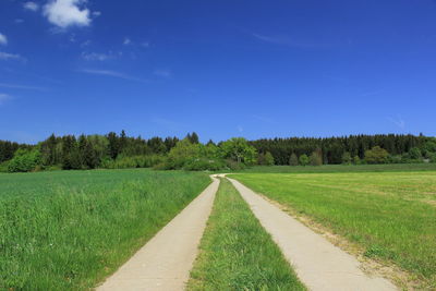 Road amidst field against clear blue sky