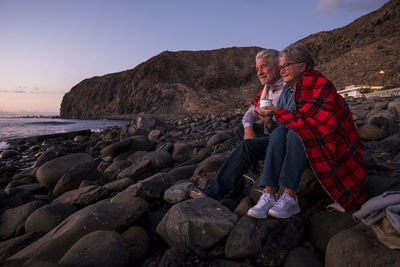 Couple sitting on rocks against sky at beach