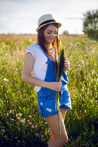 Portrait of young girl in overalls and a hat, standing with cane in hand in field