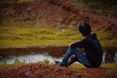 Rear view of man sitting by lake