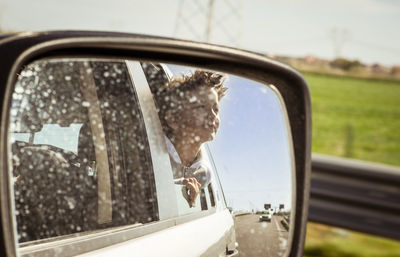 Boy reflecting on side-view mirror of car