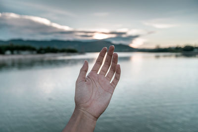 Cropped hand against lake during sunset