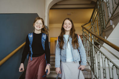 Portrait of happy female friends standing on staircase of school building