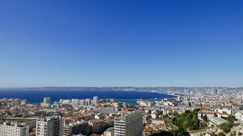 High angle view of townscape by sea against blue sky