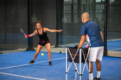 Monitor teaching padel class to woman, his student - trainer teaches young girl how to play paddle