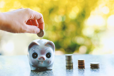 Cropped hand putting coin on piggy bank on table