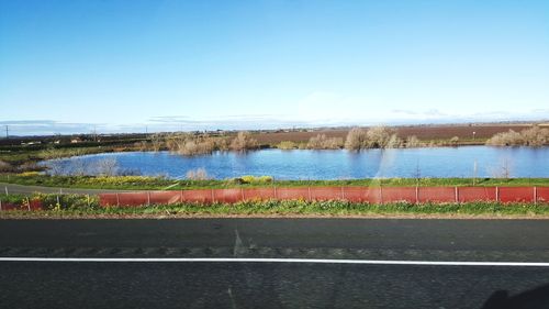 Road by lake against clear blue sky