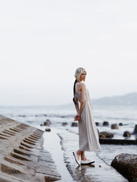 Rear view of woman standing at beach against sky