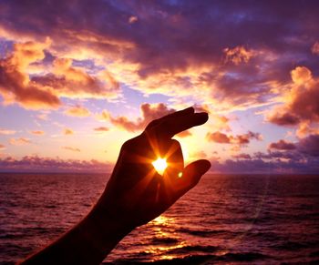 Close-up of silhouette hand against sea during sunset