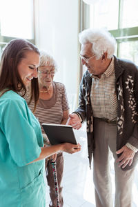 Young female nurse showing digital tablet to senior couple at nursing home