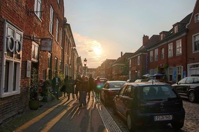 People walking on street in city against sky at sunset