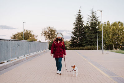 Woman with dog walking on walkway against sky