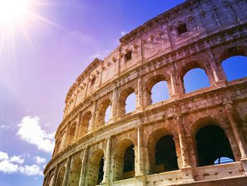 Low angle view of rome colosseum against sky with sun