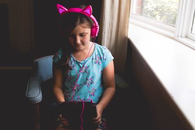 High angle view of girl using digital tablet while listening to pink headphones at home