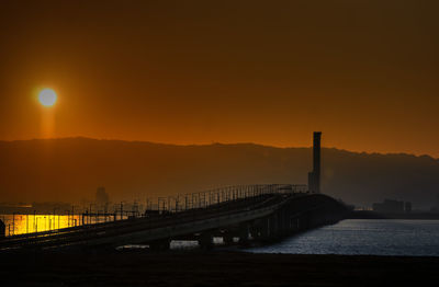 Bridge over sea against sky at sunset