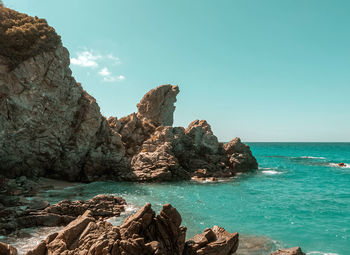 Rocks on shore by sea against blue sky