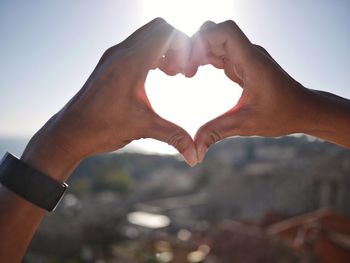 Cropped image of man making heart shape against sky