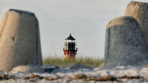 Lighthouse amidst rocks on field against sky