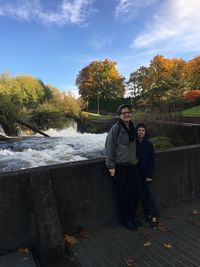 Portrait of smiling woman with son standing against river during autumn