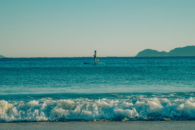 Man paddleboarding in sea against clear sky on sunny day