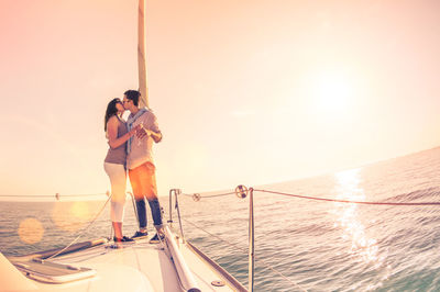 Romantic couple kissing while standing on boat in sea against clear sky during sunset