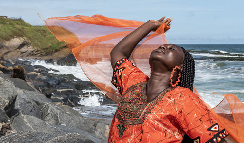African woman with orange dress on the cliffs by the sea in sekondi-takoradi ghana west africa