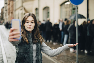 Girl taking selfie through smart phone while standing against crowd in city