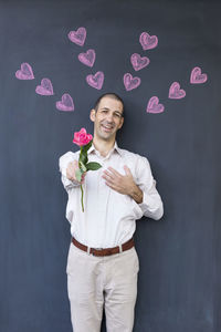 Portrait of man holding rose while standing against blackboard