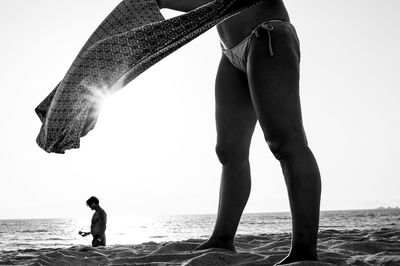 Low section of woman wearing bikini standing at beach against clear sky