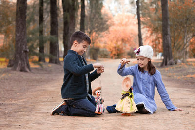 Friends playing with puppets while sitting in forest during autumn