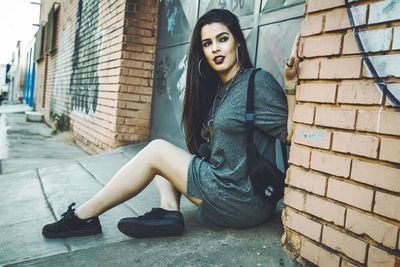 Portrait of young woman sitting on brick wall