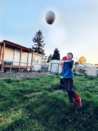 Full length of boy playing with volleyball on field against sky