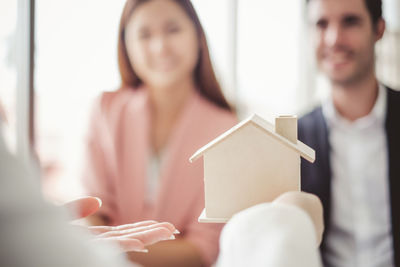 Cropped hand holding model home in front of smiling colleagues at office