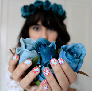 Woman with nail art holding artificial blue roses against wall