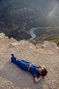 Boy child in a blue linen jumpsuit lies on the cliff of the sulak canyon in dagestan