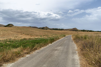 Dirt road amidst field against sky