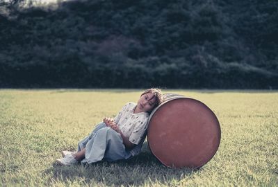 Woman sitting on grassy field by container