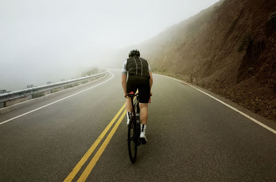 Man cycling on road by mountain during foggy weather
