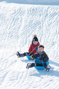 Happy siblings sledding on snow covered field during winter