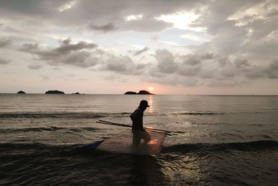 Silhouette person standing in sea against sky during sunset