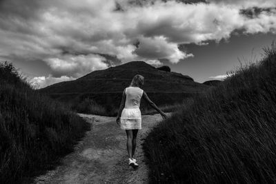 Rear view of woman walking in field against cloudy sky