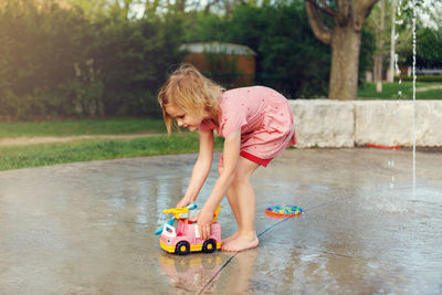 Little kid playing with toys at splash pad playground in summer. child at water park with fountains