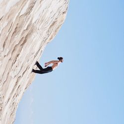 Low angle view of man perching on tree against clear sky